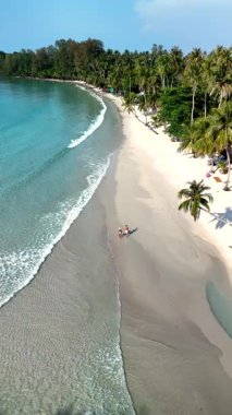 Koh Kood Island in Thailand with its crystal-clear waters and soft sandy beaches. The tranquil shoreline features palm trees, inviting visitors to relax and unwind. a couple on the beach walking
