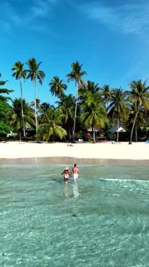 Two people, an asian woman and a caucasian men, enjoy the crystal-clear waters of Koh Kood Island, surrounded by lush palms and a tranquil beach. Perfect for a relaxing getaway in Thailands paradise.