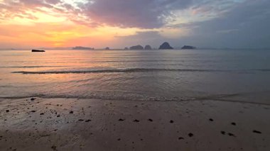 Breathtaking sunset illuminates the calm waters of Krabi, Thailand. Gentle waves lap against the sandy shore, creating a peaceful atmosphere perfect for relaxation and reflection.