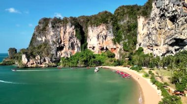 Beauty of Krabi Thailand, featuring stunning cliff formations and soft sandy beaches. Visitors enjoy the crystal-clear waters, lush greenery, and vibrant boats along the shore. Tonsai beach