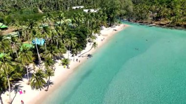 Experience the tranquil beauty of Koh Kood, Thailand, with its pristine white sand beaches and clear turquoise waters. Sunbathers relax under palm trees, creating a serene tropical atmosphere.