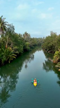Explore the tranquil beauty of Thailands rivers as a kayaker paddles through calm waters, embraced by verdant trees and tropical foliage. v couple in a kayak on a river with palm trees in Chumphon