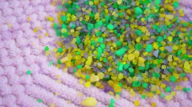 Pembe havluda çok renkli deniz tuzu kristalleri. Sert ve yumuşak arasındaki zıtlık. Farklı şekillerde yeşil ve sarı deniz tuzu kristalleri ve dokuları ışıkta parlayarak yanardöner etkiler yaratır..