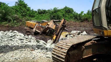 Afrika 'daki bir yağmur fırtınasından sonra tropikal bir bataklıkta sıkışmış güçlü bir kazıcı. Makine, kendi izlerini emen ıslak çamurdan kurtulamıyor ve aşırı koşullarda dramatik bir inşaat çalışması sahnesi oluşturuyor..                    