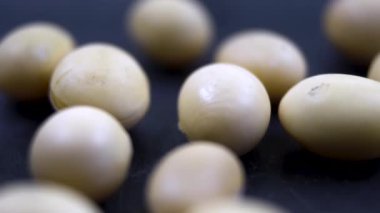 Soya fasulyesine yakın çekim. Koyu arkaplanda açık bej soya taneleri. Vejetaryen diyeti için doğal yiyecek. Orta soya fasulyeleri keskin bir şekilde odaklanırken, arka plan hafifçe bulanıklaşıyor ve derinlik yaratıyor.. 