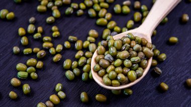 Olgun yeşil mung fasulyelerine yakın çekim. Tahta kaşıkta parlak oval tohumlar.