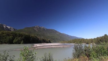 Mavi gökyüzü ve dağlarla güneşli bir günde vahşi bir nehir