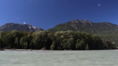 Şiddetli bir rüzgar eserken hızlı akan nehir, ağaçlar ve dağlarla birlikte.