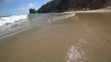 Experience beauty of sun-drenched beach in slo-mo, with waves washing over sand