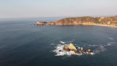 Fly over rocky outcropping juts into deep blue ocean waters.