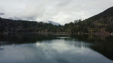 Sakin orman tepe örtüsü arasında bulutlarla çevrili bir gölün hava keşfi.