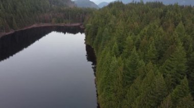 Durgun doğada süzülen bir göl ve bulutların altında yuvarlanan yeşil tepeler.