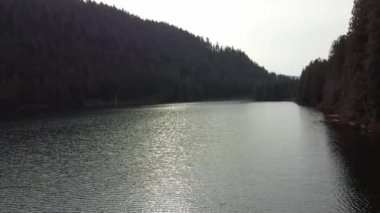 Bulutlu bir günde yeşil dağlarla çevrili huzurlu bir gölün güzelliğini keşfediyorum.