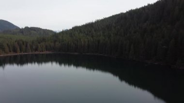 Bulutlu gökyüzünün sakinliği ve bereketli ormanlar huzurlu bir göle yansıyor.