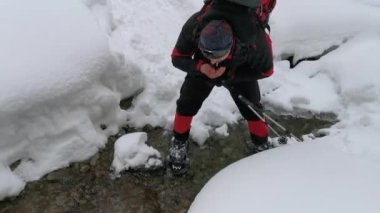 Sırt çantalı bir adam kış yürüyüşünde dereden su içiyor.. 
