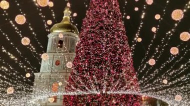Ukrayna, Kiev 'deki Sofievskaya Meydanı' nda Noel festivali ve Noel ağacı. St. Michael Katedrali uzaktan aydınlatılır. Kaygan yolda arabalar yavaşça geçer.. 