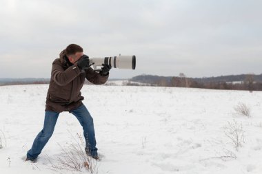 Büyük bir telefoto lensi olan bir adam fotoğraf çekmeye hazır.