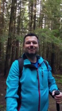 Elinde izleme direği olan bir adam ormanda selfie çekiyor. Çevreyi göstermek için dönüyor.