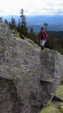 Bir kadın kayaların üzerinden dağa tırmanıyor. Yürüyüş sopaları kullanıyor..