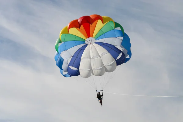 Bir kişi su yüzeyinde bir tekne tarafından tutulan bir paraşüte bağlı olarak havaya yükselir. Parasailing