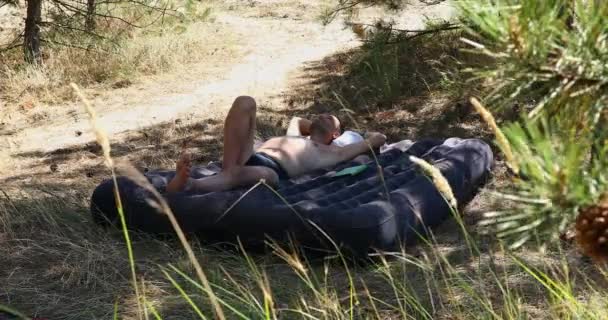 在一个阳光灿烂的夏日里 一个穿着游泳裤的男人躺在空气床垫上 他享受大自然的宁静 沐浴在温暖的阳光下 在野蛮的假期里稍纵即逝 — 图库视频影像