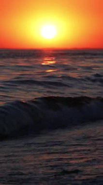 Denizde güzel bir gün batımı. Turuncu gökyüzü. Dalgalar sahile çarpar ve yaz güneşinde süzülür..