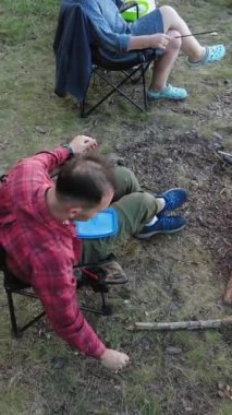 İnsanlar, turkuaz göl manzaralı bir kamp ateşinin yanında çadır kurmaktan hoşlanırlar. Dikey Video