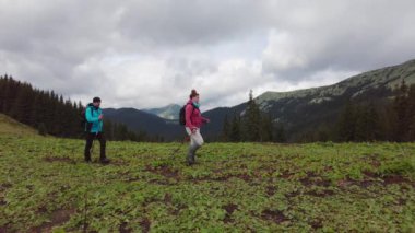 Bir adam ve bir kadın dağ manzarasının önünde yürüyüş yapıyorlar..