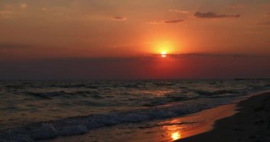 Denizde güzel bir gün batımı. Turuncu gökyüzü. Dalgalar sahile çarpıyor ve yaz güneşinde su sıçrıyor. Çekim ayarlanıyor