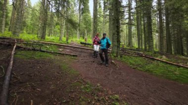 Bir adam ve bir kadın yürüyüş direkleri ile bir orman yolunda yürürken