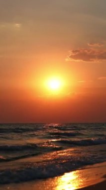 Deniz kıyısında altın bir günbatımı batan güneş kumlu kıyıya vuran dalgalara yansıyor.. 