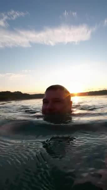 男は夜明けに澄んだ水の湖で泳いでいる バーティカルビデオ — ストック動画