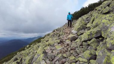 Yaya direkleri olan bir adam dağlarda kayalık bir yolda yürüyor..