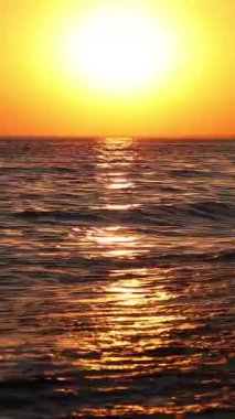 Batan güneşin ışınlarında güzel bir deniz manzarası. Dalgalar kıyıya vuruyor turuncu bir günbatımının güneşli yolunda.