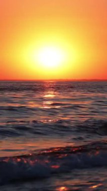 Denizde güzel bir gün batımı. Turuncu gökyüzü. Dalgalar sahile çarpar ve yaz güneşinde süzülür..