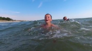 İki erkek çocuk denizde yüzüyor. Deniz dalgalarının ve güzel havanın tadını çıkarıyorlar..