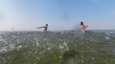 Genç bir çift denizde birbirlerinin üzerine su sıçratır. Ağır çekim. Tatil ve deniz. Su oyunları