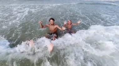 Bir adam, bir çocuk ve köpekleri deniz dalgalarında ağır çekimde yüzüyorlar.. 