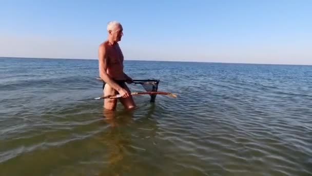 自家製の槍と網を使用して浅い水に黒海を刺す男 — ストック動画