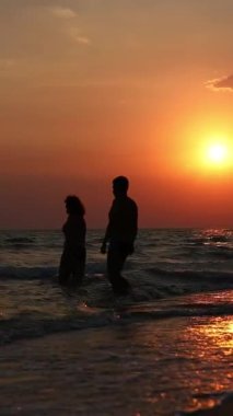 Bir adam ve bir kadın güzel bir günbatımının arka planında denize doğru yürür.