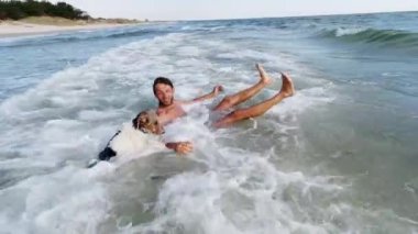 Okyanus kenarında aile tatili. Bir baba, oğlu ve köpekleri dalgalarda eğleniyor..