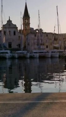 Bir kadın, sabahın erken saatlerinde marinaya bağlı yatları olan pitoresk bir Hırvat kasabasının setinde yürüyor. Dikey Video