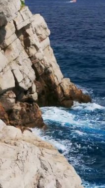 Adriyatik Denizi 'nin dalgaları güneşli bir yaz gününde kayalık sahilde kırılıyor. Dikey Video
