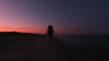 Sırt çantalı bir adam sabahın erken saatlerinde denizin kenarında yürüyor.