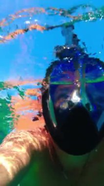 Maskeli adam denizdeki su yüzeyinde yüzüyor. Suyun altına bak. Dikey Video