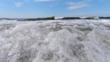 Bir deniz dalgası kıyıya vurur ve beyaz sulara karışır. Yavaş çekim, okyanus, dalgalar