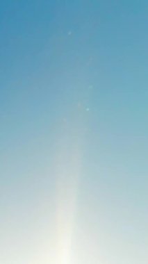 Mavi gökyüzü ve ona karşı parıldayan güneş ışığı. Dikey Video