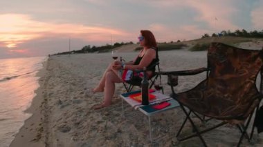 Deniz kıyısında şarap içen ve güzel günbatımını seyreden bir kadın.