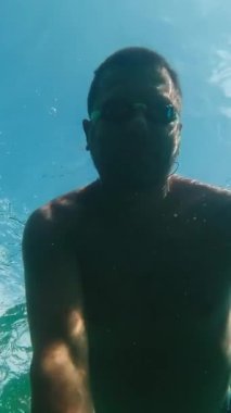 Gözlüklü bir adam denizin su yüzeyinde yüzer ve kendini suyun altından filme alır. Dikey Video