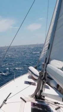 Yacht Under Sails Speeds Across the Sea Toward the Horizon on a Sunny Summer Day. Vacation and Yachting Sport. Vertical Video
